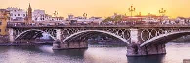 Puente de Triana al atardecer con tonos cálidos y siluetas de edificios sevillanos