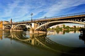 Puente de Triana reflejado en las aguas del río bajo un cielo despejado