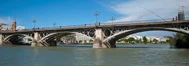 Vista panorámica del Puente de Triana sobre el río Guadalquivir con cielo azul y edificios al fondo
