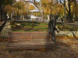 Estatua junto a un banco con kiosco al fondo en otoño