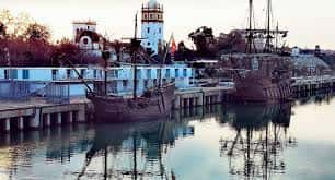 Escenario festivo en el muelle con réplicas de naves históricas y ambiente de celebración