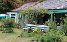 Casa con porche y jardín lleno de plantas y bancos