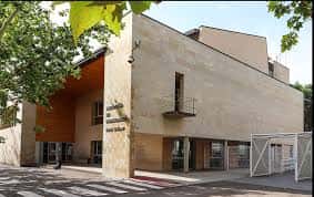 Exterior de la biblioteca con árboles y acceso principal bajo un cielo despejado