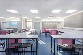Interior de un aula o espacio de trabajo con mesas altas y sillas en tonos rosa y azul