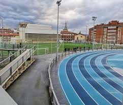 Detalle de la pista de atletismo azul con gradas y edificios urbanos al fondo