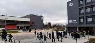 Plaza principal del campus con estudiantes y edificios modernos bajo cielo nublado