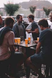 Clientes sentados en terraza exterior tomando cervezas en mesas altas