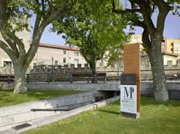 Entrada exterior del Museo de las Termas Romanas con señalización y entorno ajardinado
