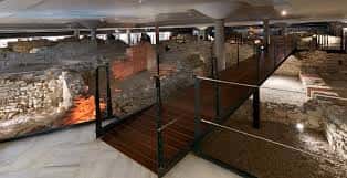 Pasarela de madera sobre las ruinas romanas con barandillas de cristal y suelo de mármol