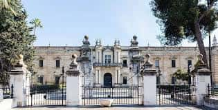 Exterior de la Real Fábrica de Tabacos con jardín delantero y árboles, mostrando la simetría arquitectónica