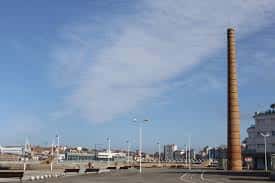 Chimenea de Poniente destacando sobre el paseo marítimo y el mar al fondo en día despejado