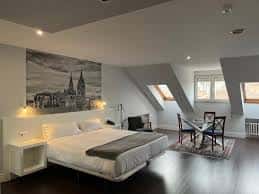 Suite con techo inclinado, cama king-size y vista panorámica de Oviedo en el mural