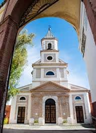 Vista exterior de la Parroquia de la Santísima Trinidad desde un arco, mostrando su fachada clásica y campanario