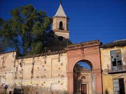 Fachada lateral de la parroquia con torre campanario y arco de acceso bajo cielo azul