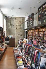 Interior de la Librería Proteo con estanterías llenas de libros y una pared de mampostería histórica visible
