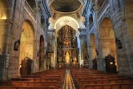 Interior de la nave central de la iglesia con bancos de madera y altar iluminado