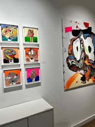 Pared de la galería con múltiples cuadros de arte moderno y una obra grande