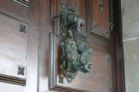 Primer plano del portón de madera con herrajes ornamentales y escudo en relieve