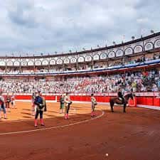 Escena de festejo taurino con banderilleros y caballo en el ruedo