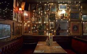 Área íntima del local con paredes decoradas con cuadros y luces cálidas, ideal para eventos pequeños o cenas privadas