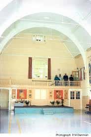 Interior del gimnasio o salón de actos con arco blanco, escenario y galería superior