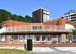 Vista del ala curva del colegio con balcón y entorno urbano al fondo