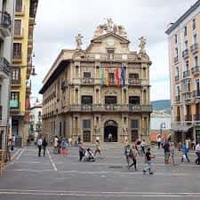 Vista frontal del Ayuntamiento de Pamplona en la Plaza del Castillo con banderas y peatones