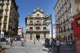 Plaza del Castillo con el Ayuntamiento al fondo, personas caminando y bicicletas en un día soleado
