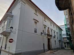 Vista exterior de la Casa da Veeduría en A Coruña, mostrando su fachada blanca y detalles arquitectónicos
