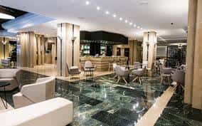 Lobby principal del hotel con suelo de mármol verde, columnas y zona de recepción