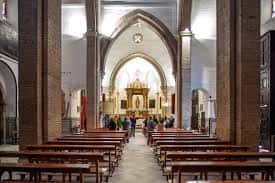 Interior de la iglesia con naves centrales, bancos de madera y altar principal iluminado
