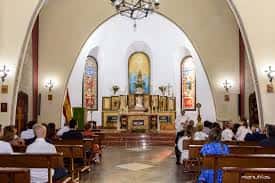Interior de la parroquia durante una ceremonia religiosa con fieles sentados en bancos y altar central decorado