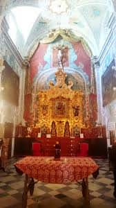 Altar mayor de la parroquia con retablo dorado, pintura mural y mesa de comunión cubierta con mantel rojo