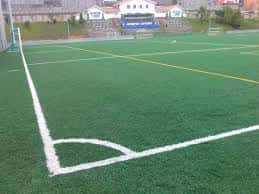 Campo de fútbol con césped artificial y gradas al fondo