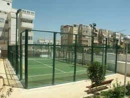 Pista de pádel al aire libre con vallas verdes y entorno urbano