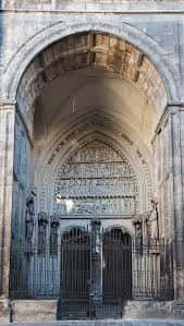 Puerta principal gótica con arco decorado y reja metálica