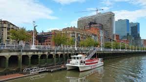 Embarcadero de Pío Baroja con un barco turístico atracado y edificios modernos al fondo