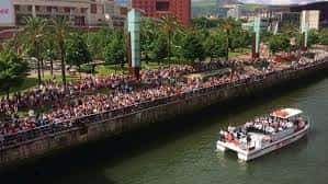 Vista aérea del embarcadero lleno de gente y un barco navegando por la ría