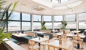 Interior del restaurante con mesas dispuestas para eventos y grandes ventanales con vistas al mar
