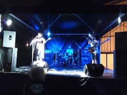 Escenario interior del pabellón durante un evento con iluminación azul y artistas en actuación