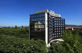 Fachada moderna del hotel rodeada de árboles bajo un cielo azul