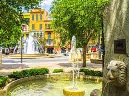 Vista panorámica de la plaza con fuentes, edificios coloridos y vegetación