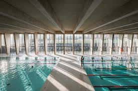 Piscina interior del polideportivo con luz natural y estructura de vigas en el techo