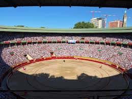 Vista desde las gradas superiores de la Plaza de Toros de Pamplona con la plaza llena y edificios al fondo