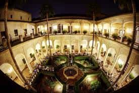 Patio interior iluminado con jardín central y arquerías, ideal para eventos nocturnos