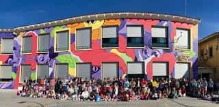 Grupo de estudiantes y personal frente al edificio con mural colorido