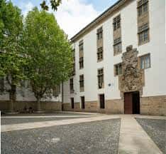 Vista exterior del patio de la Facultad de Filosofía con fachada blanca y escudo heráldico