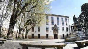 Fachada principal de la Facultad de Filosofía con estatua y árboles en primer plano