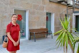 Mujer sonriendo frente a la entrada lateral del centro, con planta decorativa y banco de madera