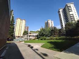 Área verde del parque con edificios residenciales al fondo bajo cielo despejado